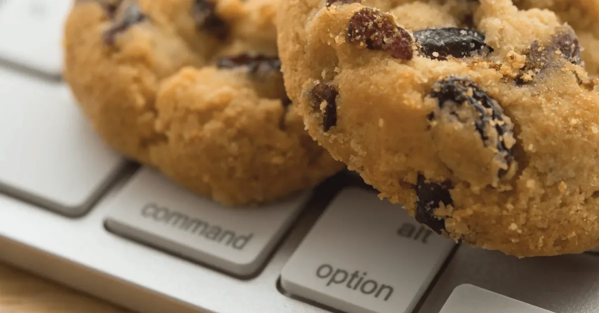 Two chocolate chip cookies resting on a laptop keyboard