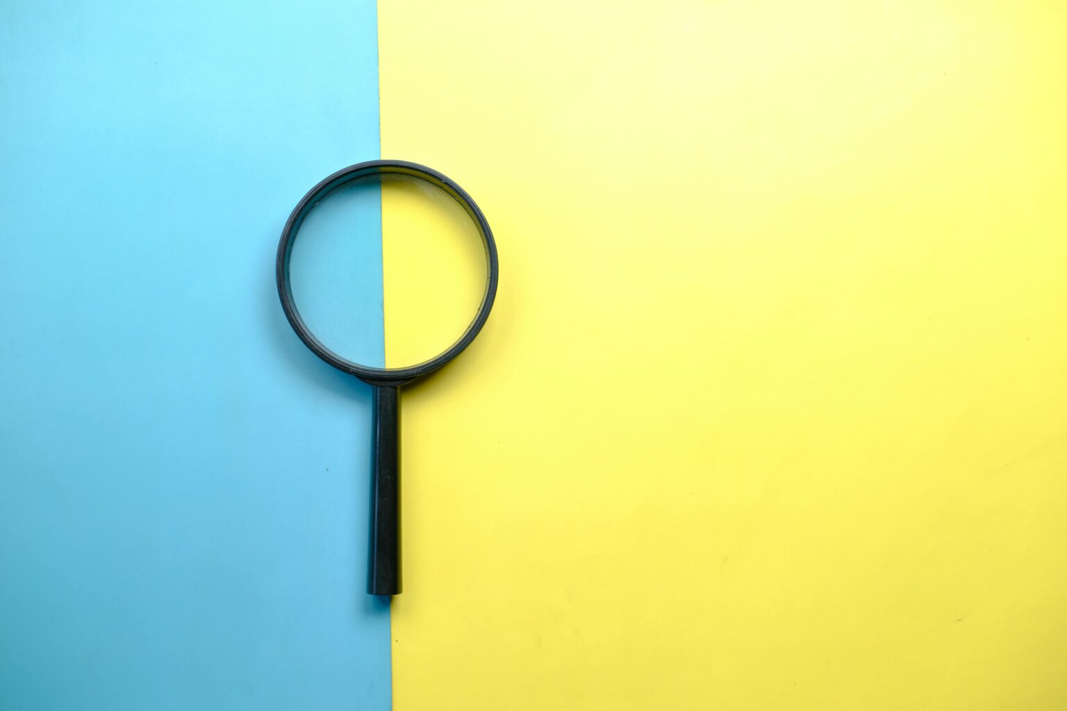 A magnifying glass resting on a two-tone blue and yellow background